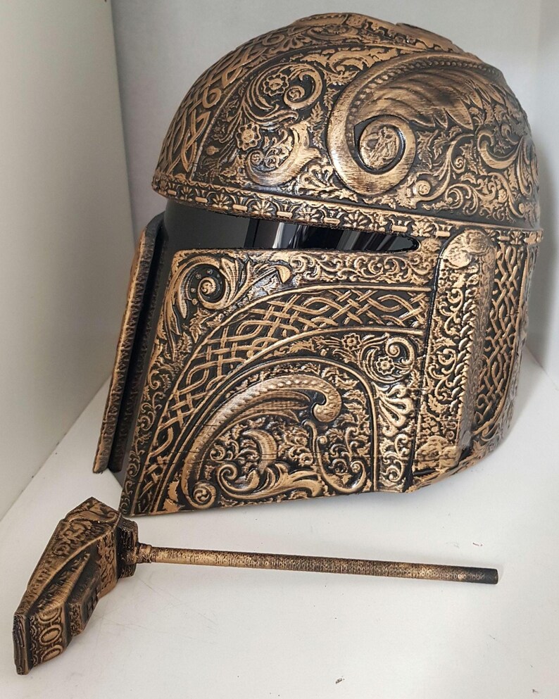 Op de afbeelding: Een gouden en zwarte helm met ingewikkelde bloem- en Keltische knoopontwerpen. De helm is gemaakt van een hard materiaal en heeft een vizier. De helm is een rekwisiet voor cosplay of kostuum.