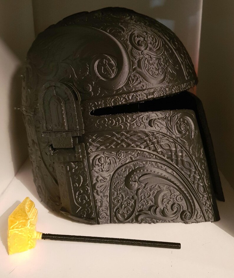 Op de afbeelding: Een zwarte helm met ingewikkelde, sierlijke ontwerpen. De helm is gemaakt van een 3D-geprint materiaal en heeft een vizier.