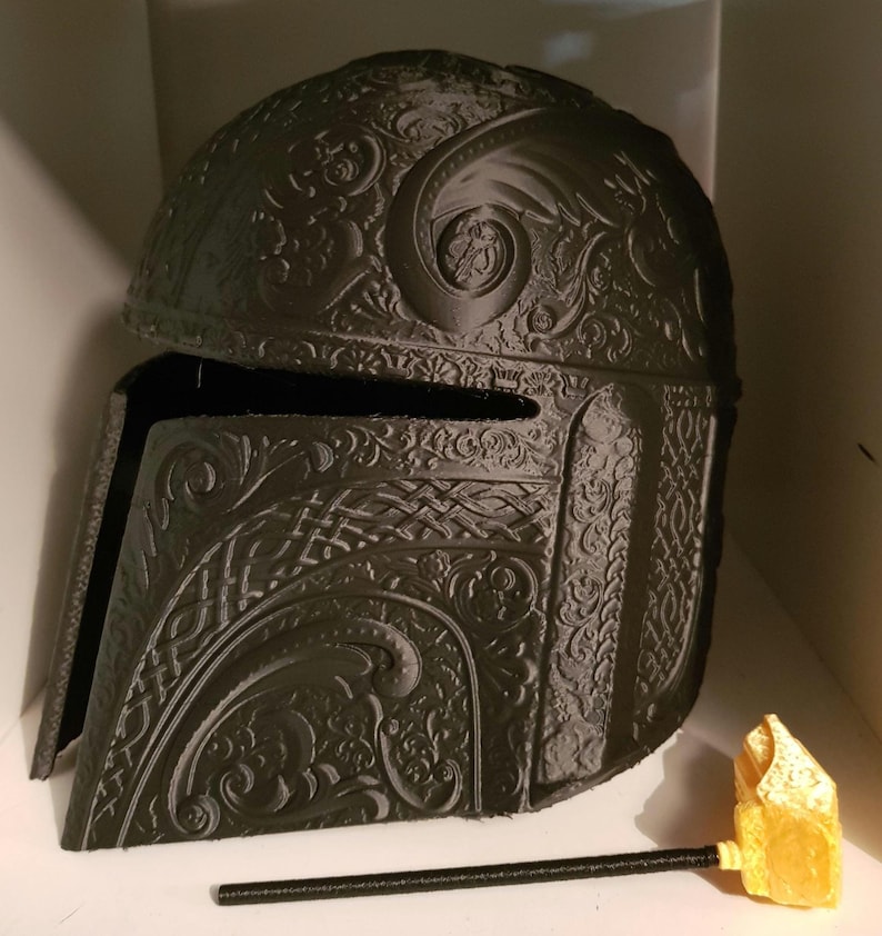 Op de afbeelding: Een zwarte 3D-geprinte helm met ingewikkelde bloem- en geometrische ontwerpen. De helm heeft een vizier en een puntige bovenkant.