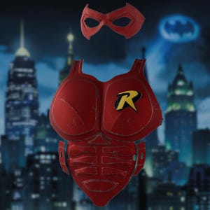 Puede incluir: Una pieza de armadura de pecho roja con un emblema R amarillo y negro en el lado izquierdo, con detalles abdominales moldeados y un antifaz rojo a juego. La armadura tiene un acabado texturizado y está diseñada para cubrir el torso completo.