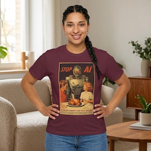 May include: A maroon t-shirt featuring a vintage-style graphic print of a robot standing between a man and a woman at a dinner table with a roasted turkey. The text at the top reads STOP AI, and the bottom text reads DEFEND OUR HUMANITY.