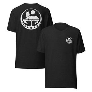 Op de afbeelding: Twee donkergrijze t-shirts met een wit grafisch ontwerp. Het ontwerp toont een gestileerde wolf- of hondfiguur, een maan en sterren in een cirkelvormig frame. Eén shirt toont het ontwerp op de voorkant, de andere op de achterkant.