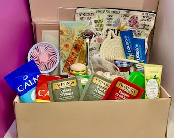 May include: A gift box containing a variety of items including Twinings Prince of Wales and English Breakfast tea bags, a blue Calm snack bag, a small pink fan, a pouch with inspirational text, Liquid I.V. packets, olive hand cream, and honey.