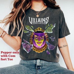 Puede incluir: Camiseta gris oscuro con la palabra "Villains" sobre un dise&ntilde;o de espejo roto con una m&aacute;scara morada y amarilla. El texto "Unfairly Ever After" est&aacute; debajo. Es una camiseta c&oacute;moda.