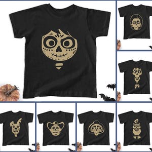 May include: Black t-shirts with various beige-colored skull designs. The designs include a skull face, a skull with a bow tie, and other stylized skull illustrations. The shirts are displayed with a pumpkin and bat decorations.