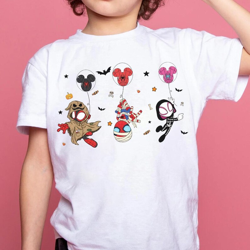 Puede incluir: Camiseta blanca con personajes de dibujos animados de Halloween. El dise&ntilde;o incluye un fantasma, una momia y una figura similar a Spider-Man, cada uno suspendido por globos. Murci&eacute;lagos, estrellas y caramelos completan el dise&ntilde;o. Una camiseta gr&aacute;fica divertida y colorida para ni&ntilde;os.