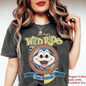 May include: Dark gray t-shirt featuring a cartoon image of Mr. Toad from Mr. Toad's Wild Ride. The design includes the text "Mr. Toad's Wild Ride" and "Semper Toadi Acceleratio Absurda". The shirt is a pepper color and is a comfort tee.