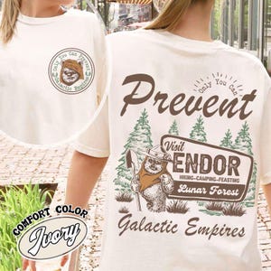 Könnte beinhalten: Elfenbeinfarbenes T-Shirt mit einer Grafik, die einen Ewok mit einer Schaufel, den Text "Visit Endor" und "Galactic Empires" zeigt. Das Shirt hat auch den Text "Only You Can Prevent" und "Lunar Forest".