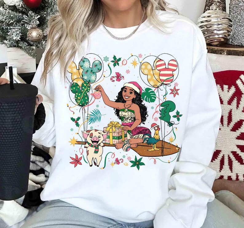 K&ouml;nnte beinhalten: Wei&szlig;es Sweatshirt mit einer farbenfrohen Grafik eines Cartoon-Charakters mit Weihnachtsm&uuml;tze, umgeben von Luftballons, Geschenken und festlichen Dekorationen. Das Design umfasst ein Schwein, ein Huhn und Mickey Mouse-f&ouml;rmige Luftballons. Ein grafisches T-Shirt zum Thema Feiertage.