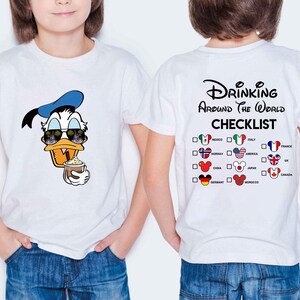 May include: White t-shirt featuring a cartoon Donald Duck wearing sunglasses and a blue hat, holding a drink. The back of the shirt has the text "Drinking Around The World Checklist" with country flags.