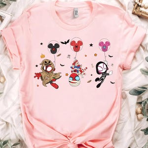 Puede incluir: Camiseta rosa claro con personajes de dibujos animados disfrazados para Halloween. Los personajes cuelgan de globos con forma de Mickey Mouse y Spider-Man. Murci&eacute;lagos y estrellas est&aacute;n dispersos.