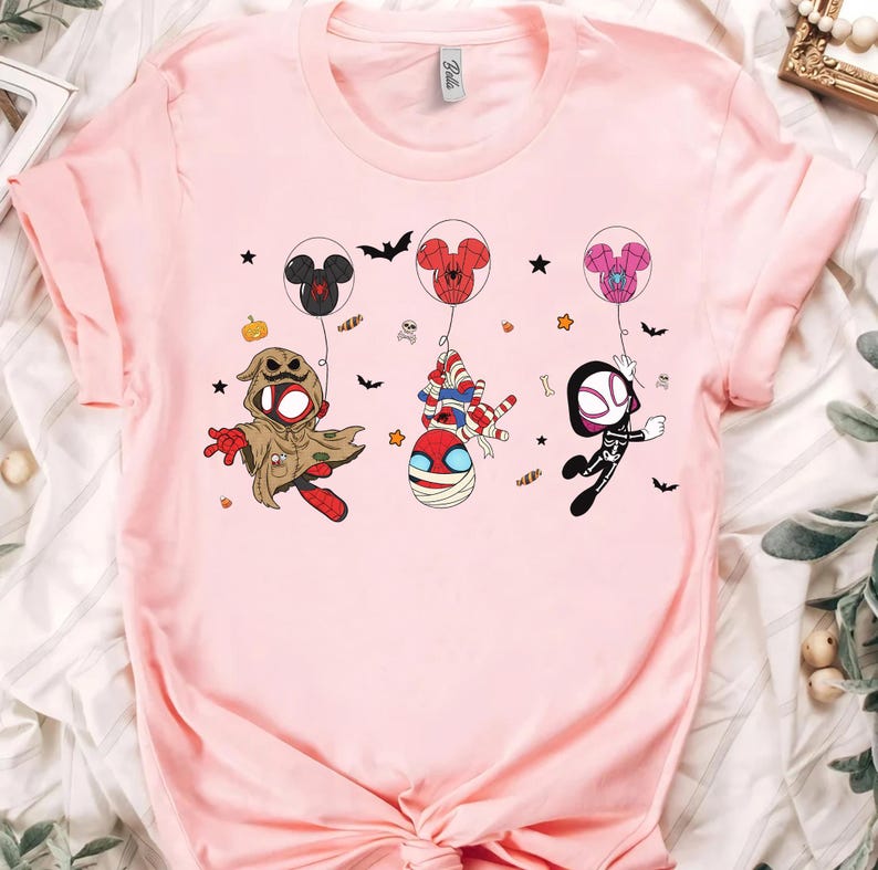 Puede incluir: Camiseta rosa claro con personajes de dibujos animados disfrazados para Halloween. Los personajes cuelgan de globos con forma de Mickey Mouse y Spider-Man. Murci&eacute;lagos y estrellas est&aacute;n dispersos.