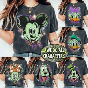 Puede incluir: Una camiseta gris carbón de manga corta con un gráfico de una cara de personaje de dibujos animados verde, cosida con puntos y un fondo de telaraña. La camiseta muestra el texto WE DO ALL CHARACTERS en una fuente verde desgastada.