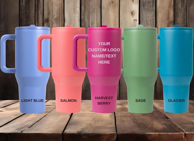 K&ouml;nnte beinhalten: F&uuml;nf hohe Isolierbecher mit Henkel in den Farben Hellblau, Lachs, Beere, Salbei und Gletscher. Der mittlere beerenfarbene Becher tr&auml;gt den Text YOUR CUSTOM LOGO NAME/TEXT HERE. Jeder Becher ist mit einem passenden Deckel und Henkel versehen.