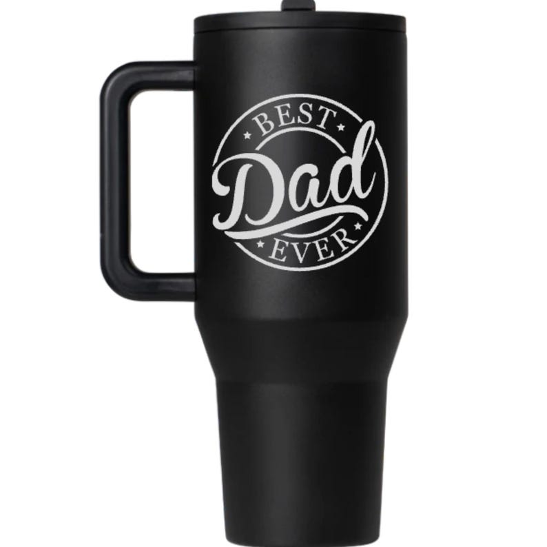 K&ouml;nnte beinhalten: Ein mattschwarzer Edelstahlbecher mit passendem Deckel und einem stabilen Seitengriff. Die Vorderseite zeigt eine wei&szlig;e kreisf&ouml;rmige Grafik mit dem Text "BEST" oben, "Dad" in gro&szlig;er Schreibschrift in der Mitte und "EVER" unten.