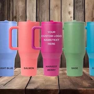Puede incluir: Cinco vasos aislados en colores azul claro, salm&oacute;n, baya de la cosecha, salvia y glaciar. Cada vaso tiene un asa y una tapa. El vaso de baya de la cosecha tiene el texto "YOUR CUSTOM LOGO NAME/TEXT HERE". La parte inferior de cada vaso tiene una etiqueta coordinada.