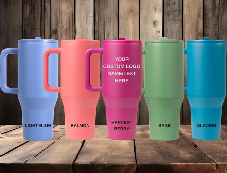 Puede incluir: Cinco vasos aislados en colores azul claro, salm&oacute;n, baya de la cosecha, salvia y glaciar. Cada vaso tiene un asa y una tapa. El vaso de baya de la cosecha tiene el texto "YOUR CUSTOM LOGO NAME/TEXT HERE". La parte inferior de cada vaso tiene una etiqueta coordinada.