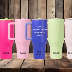 Puede incluir: Cinco vasos aislados en colores vibrantes: orqu&iacute;dea, rubor, lima rickey, mel&oacute;n y arena rosa. Cada vaso tiene un asa y una tapa. El vaso azul tiene el texto "YOUR CUSTOM LOGO NAME/TEXT HERE".