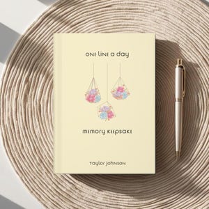 Pode incluir: Um diário amarelo com o texto "one line a day memory keepsake" e o nome "Taylor Johnson". O diário tem um design floral com três formas geométricas penduradas com flores dentro.