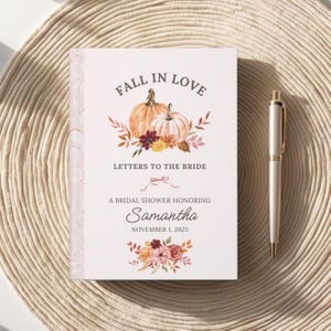 Puede incluir: Un libro de visitas personalizado para una despedida de soltera con el texto "Fall in Love" y "Letters to the Bride". La portada presenta calabazas y detalles florales. El libro está personalizado para Samantha, con la fecha 1 de noviembre de 2025. Un bolígrafo dorado descansa al lado.