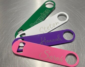 May include: Four personalized bottle openers in green, white, purple, and pink. Each opener has a different name engraved: Brandon, Steton, Hannah, and Sarah. The openers are made of metal and have a hole for hanging.