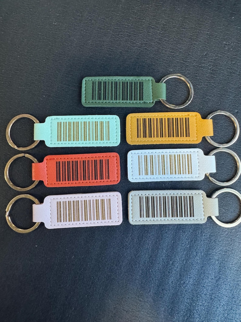 May include: Seven leather keychains with different colored backgrounds and black barcodes. The keychains are attached to silver key rings.