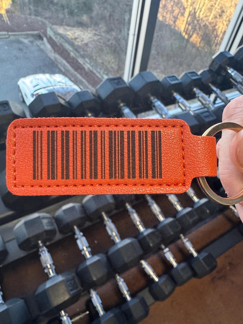 May include: Orange leather keychain with a black barcode and a silver key ring. The keychain is in focus and the background is out of focus.