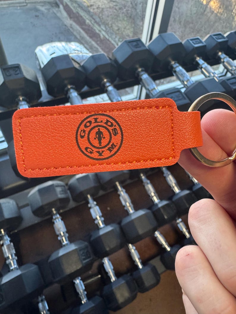May include: Orange leather keychain with a black logo that says "Gold's Gym" and a stick figure lifting weights. The keychain has a silver key ring.