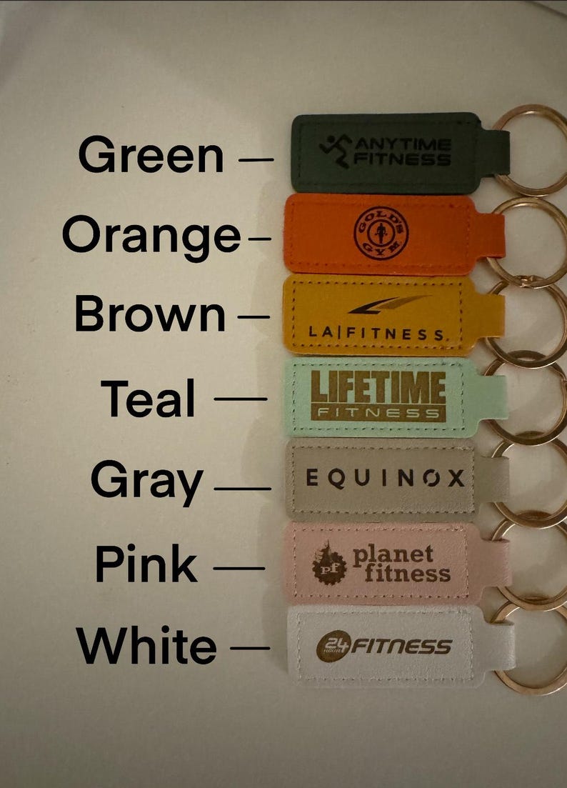 May include: Seven different colored keychains with the logos of various fitness centers. The keychains are arranged vertically from top to bottom in the following order: green, orange, brown, teal, gray, pink, and white. The logos are: Anytime Fitness, Gold's Gym, LA Fitness, Lifetime Fitness, Equinox, Planet Fitness, and 24 Hour Fitness.