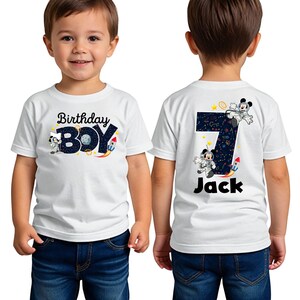 May include: White t-shirt with a space-themed design featuring Mickey Mouse as an astronaut. The front of the shirt says "Birthday Boy" and the back says "Jack" with the number 7.
