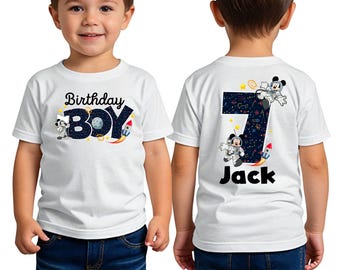 Peut inclure: T-shirt blanc avec un motif sur le thème de l'espace représentant Mickey Mouse en astronaute. Le devant du t-shirt dit "Birthday Boy" et le dos dit "Jack" avec le chiffre 7.
