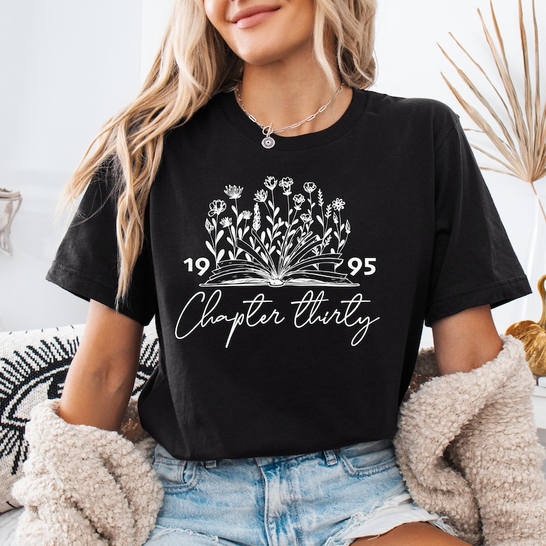 a woman wearing a black t - shirt with a graphic of a book and flowers