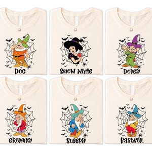 May include: Six cream-coloured t-shirts with Halloween-themed graphics. Each shirt features a different character from Snow White and the Seven Dwarfs, including Doc, Snow White, Dopey, Grumpy, Sleepy, and Bashful, with their names printed below.
