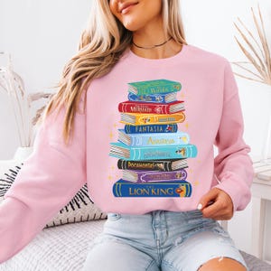 a woman wearing a pink sweatshirt with a stack of books on it