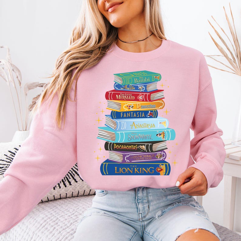 a woman wearing a pink sweatshirt with a stack of books on it
