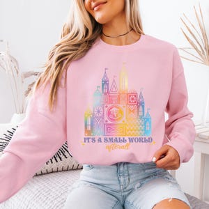 a woman sitting on a bed wearing a pink sweatshirt