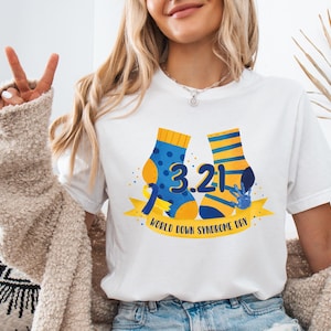 Op de afbeelding: Wit T-shirt met een afbeelding van twee sokken met de nummers 3.21 en de tekst "Wereld Down Syndroom Dag".