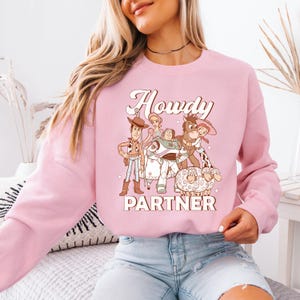 a woman sitting on a bed wearing a pink sweatshirt