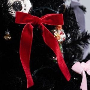 May include: A black Christmas tree decorated with a red velvet bow, a vintage clock ornament, and a pink velvet bow.