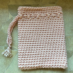 May include: A pale pink crocheted pouch with a drawstring closure. The rectangular pouch has a textured surface from the crochet stitches. The drawstring is made of the same yarn and has a tassel. The item is likely handmade.