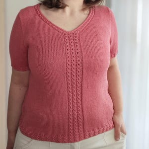 Può includere: Un top in maglia color corallo a maniche corte con scollo a V. Il top presenta un pannello traforato decorativo al centro e lungo lo scollo e l'orlo. L'indumento è realizzato con un filato morbido e strutturato.