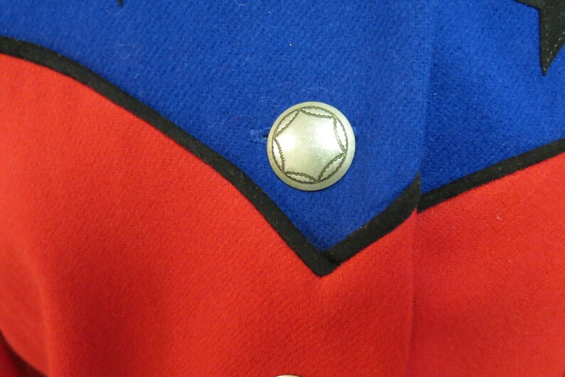May include: A close-up of a red and blue fabric with a silver star-shaped button. The button is sewn onto the blue fabric.