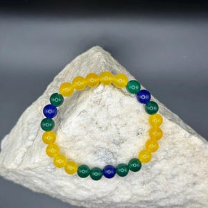 Könnte beinhalten: Ein Armband aus gelben, grünen und blauen Perlen. Die Perlen sind rund und glatt.