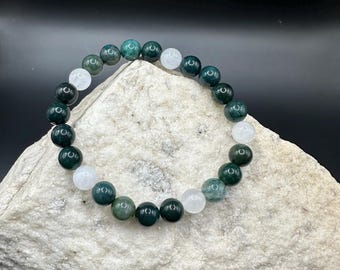 May include: A green and white beaded bracelet with alternating green and white beads. The bracelet is made of natural stones and is resting on a white rock.