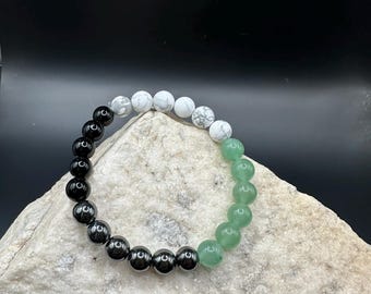 May include: A bracelet made with black, white, and green beads. The beads are round and smooth.