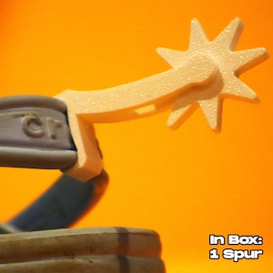 Op de afbeelding: Close-up van een beige spoor met een stervormige spoorwiel. De spoor is bevestigd aan een grijze riem. De achtergrond is effen oranje. Tekst in de afbeelding luidt "In Box: 1 Spur."