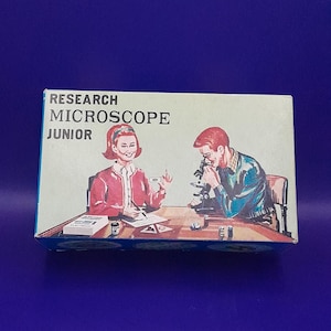 May include: A blue and white box with the text "RESEARCH MICROSCOPE JUNIOR" on the front. The box features an illustration of two children using a microscope.