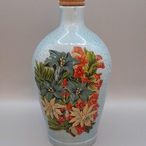 May include: A light blue ceramic bottle with a cork stopper and a floral design featuring blue, white, and orange flowers.