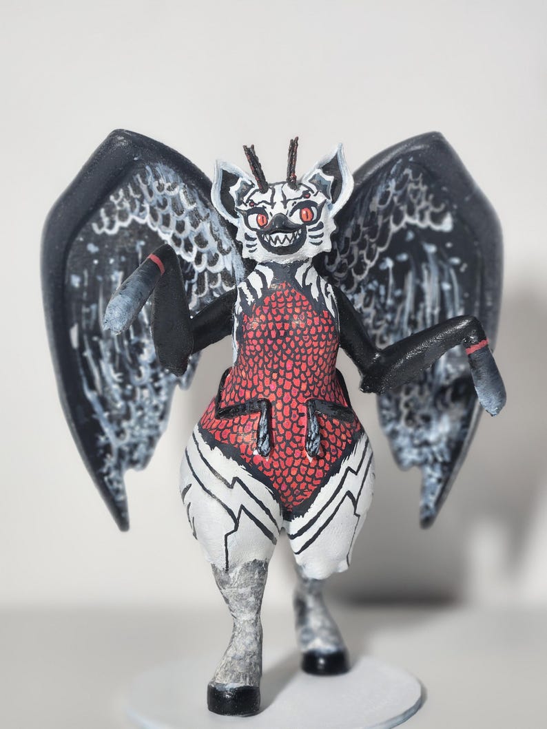 May include: A hand-painted figurine of a creature with large black wings, red eyes, and a white face with black markings. The torso features a red scale pattern, while the lower body is white with black lines. It has two small antennae.