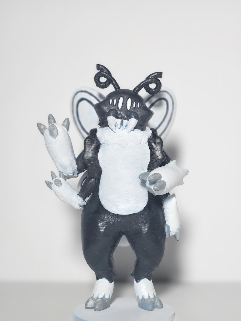 May include: A black and white creature figurine with four arms, large white fangs, multiple eyes, and insect-like wings. The figure has a textured surface, a white chest and limb accents, and stands on a circular base with a solid color background.